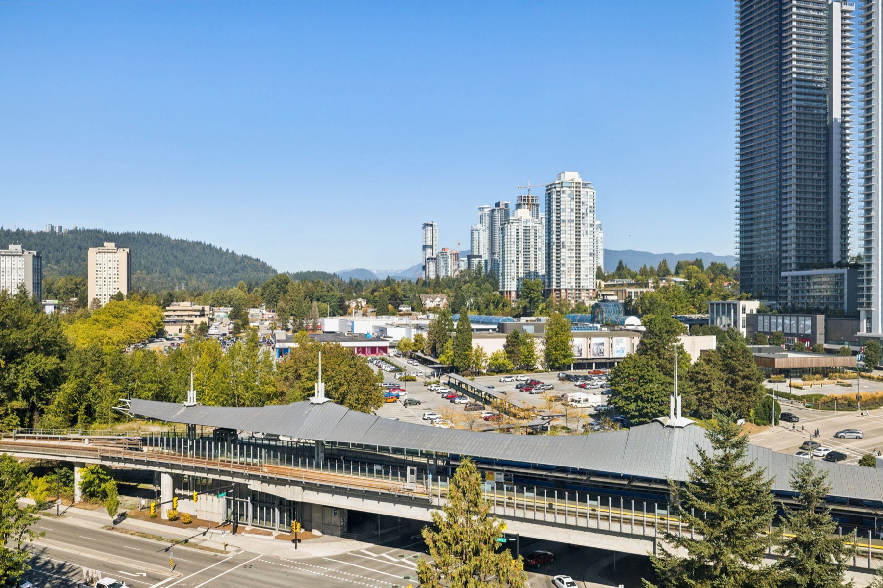 Across the SkyTrain line to the mountains, a tall tower at the edge of the frame.